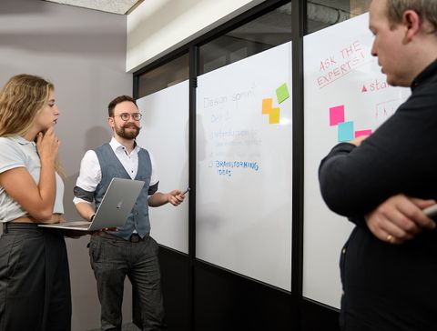 Three people having a meeting around a whiteboard