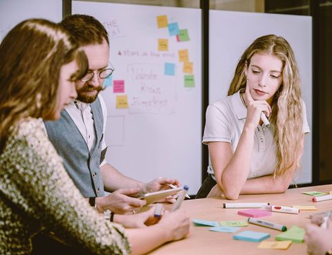 Three team members meeting in front of a whiteboard filled with colored Post-it notes.
