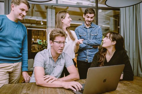 Five team members laughing around a laptop