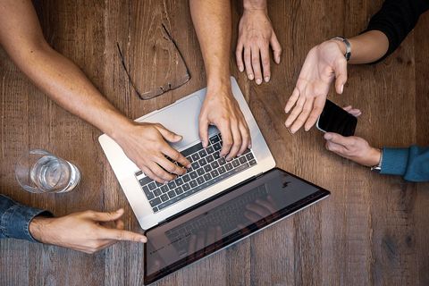 People gathered around a laptop, only their hands are visible