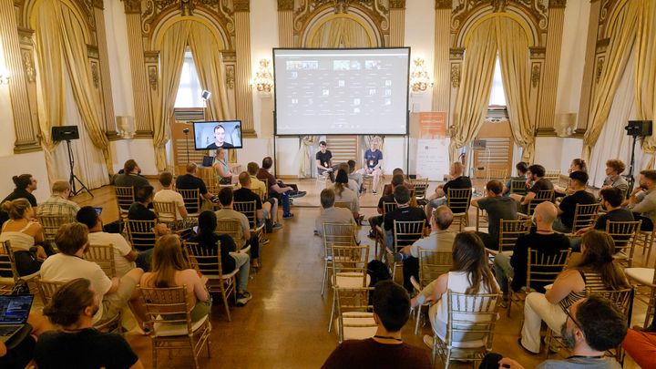 Two engineers speaking in front of a projector in front of a large audience