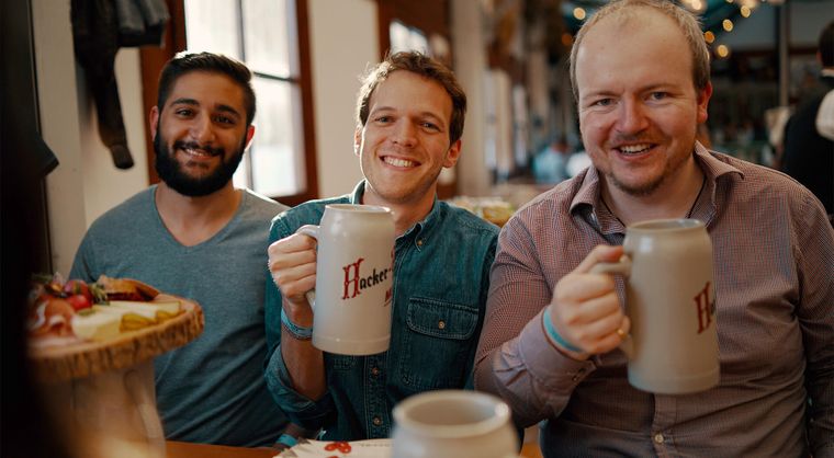 Three members of the Mainmatter team smiling at the camera, two of them are raising a glass to the viewer